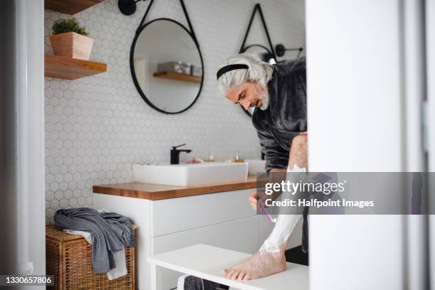 mature man in bathroom indoors at home, shaving legs. - rasieren stock-fotos und bilder