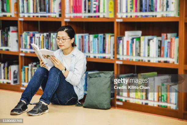 asian female adult student sitting on floor reading a book in a library - sitting on floor stock pictures, royalty-free photos & images