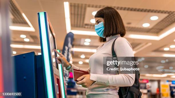female tourist wearing protective face mask and checking for her flight in airport - medical tourism stock pictures, royalty-free photos & images