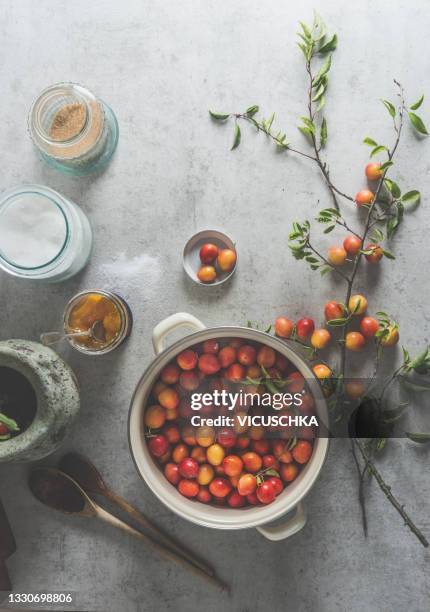 cooking pot with cherry-plum on light grey concrete kitchen table with branches, leaves and kitchen utensils - mirabelle stock-fotos und bilder