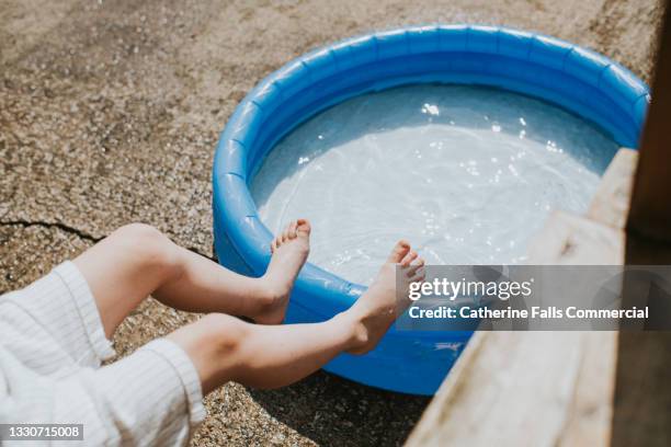 conceptual image of a child's small feet in mid air over an inflatable paddling pool on a hot day - ondata di calore foto e immagini stock