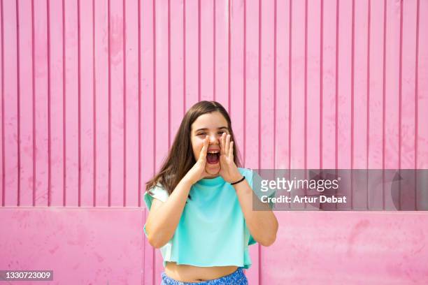 young girl shouting with summer clothes in front of pink background. - enfant crier photos et images de collection