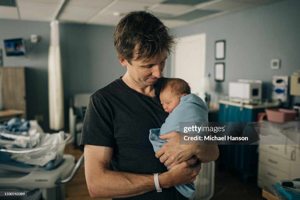A father holds his newborn son in his arms while in the hospital.