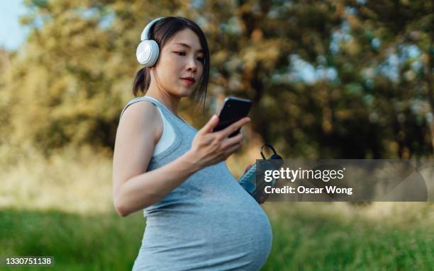 pregnant woman listening to music with headphone while walking at park - asian and indian ethnicities smartwatch phone stock pictures, royalty-free photos & images