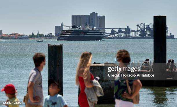 Tourists watch from Belem Ferry station the Portuguese registered "World Navigator" sailing the Tagus River after departing Lisbon Cruise Terminal...