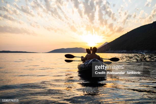 eine junge frau, die ein foto von einem perfekten sonnenuntergang macht, während sie mit ihrem freund kajak fährt - kayak stock-fotos und bilder