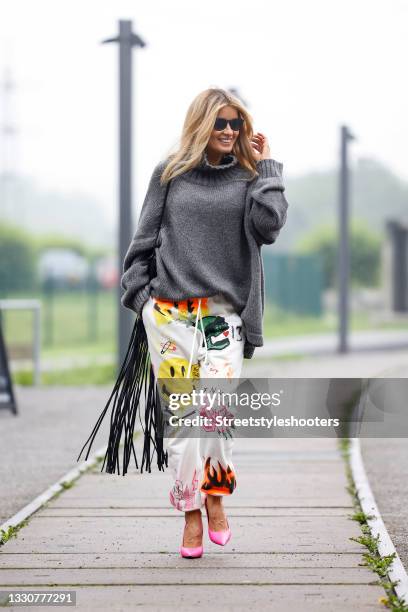 Influencer Gitta Banko wearing white sweatpants with multicolored graffiti print by R13, a dark grey knitted oversized pullover by Larens, pink pumps...