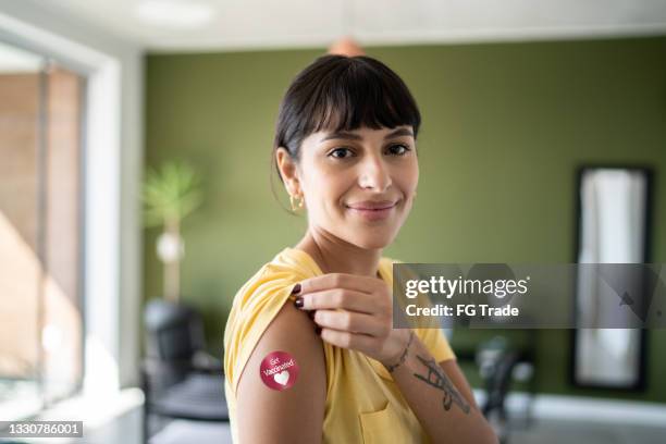 portrait of a young woman showing arm with 'got vaccinated' sticker on - rolled up sleeves stock pictures, royalty-free photos & images