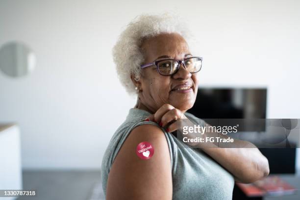 portrait of a senior woman showing arm with 'got vaccinated' sticker on - vaccine confidence stock pictures, royalty-free photos & images
