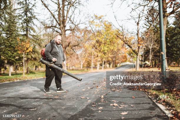 bald male worker focused on blowing leaves in park - leaf blower stock pictures, royalty-free photos & images