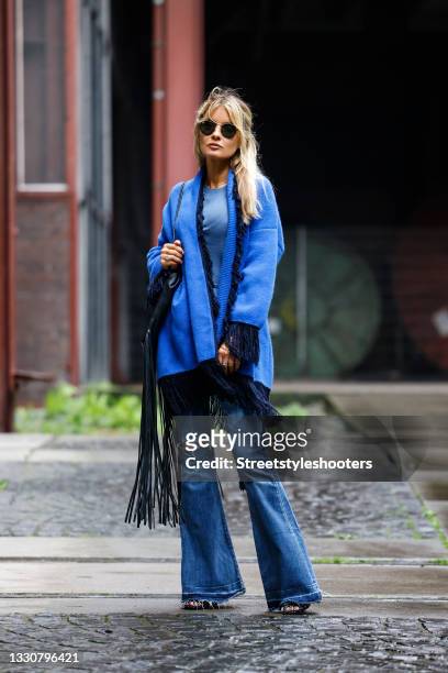 Influencer Gitta Banko wearing a blue cashmere cardigan with fringe detail by Simone Bruns, blue flared and distressed denim jeans pants by Agolde, a...