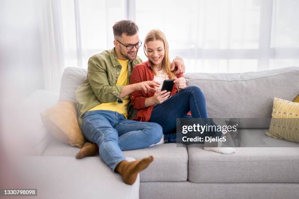 young couple surfing the net on mobile phone at home. - 年輕情侶 個照片及圖片檔