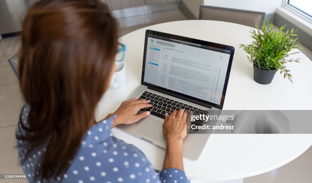 Woman telecommuting and reading her e-mail on a laptop at home