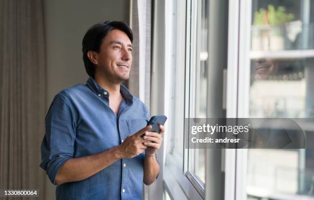 latin american man at home texting on his cell phone - talk phone flat imagens e fotografias de stock