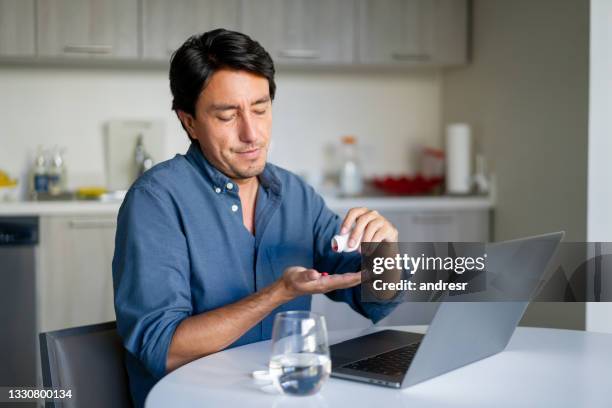 man working at home and taking pills for a headache - taking medication stockfoto's en -beelden