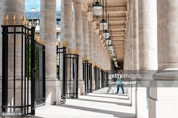 colonnade in palais royal, paris, with two people walking - palais royal stockfoto's en -beelden