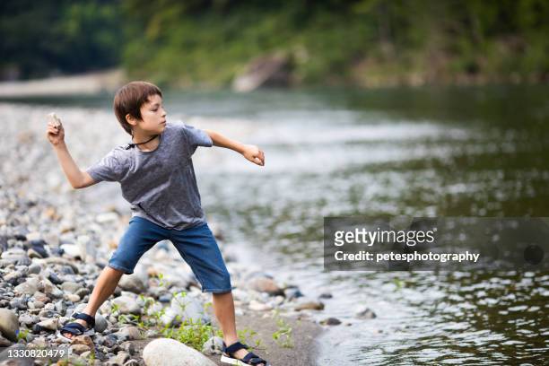 kleiner junge, der felsen an einem see überfliegt - skimming stones stock-fotos und bilder