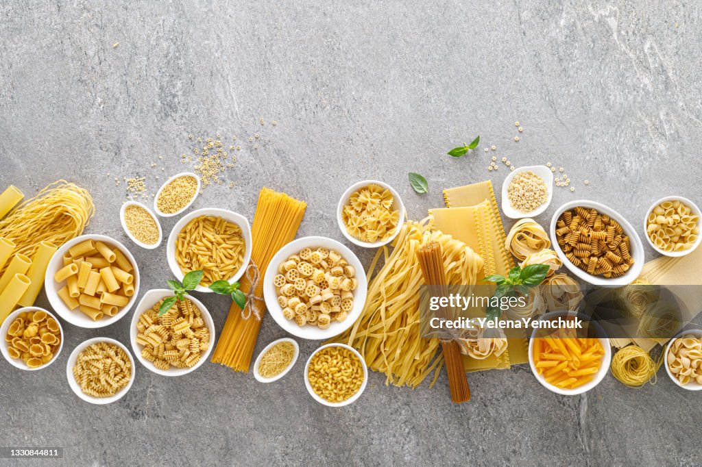 Pasta. Various kinds of uncooked pasta and noodles over stone background, top view with copy space for text. Italian food culinary concept. Collection of different raw pasta on cooking table