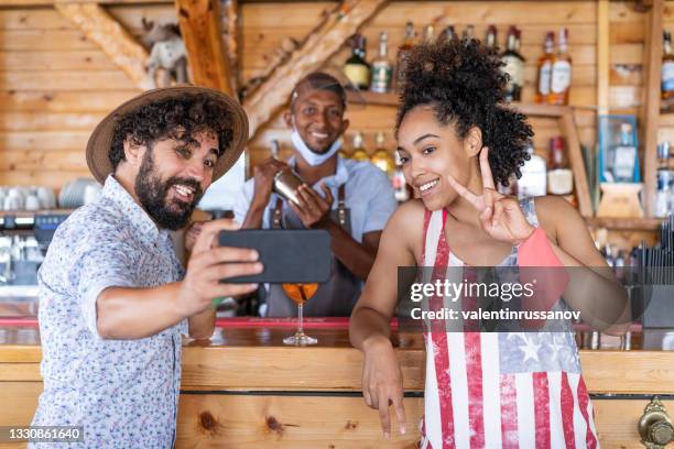 friends drinking cocktail in a restaurant bar in summer days with protective face mask and taking selfie, - bar reopening stock pictures, royalty-free photos & images