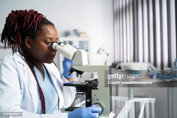 african-american scientist woman or graduate student in a lab coat and protective face mask  works in modern laboratory - doctor lab coat stockfoto's en -beelden