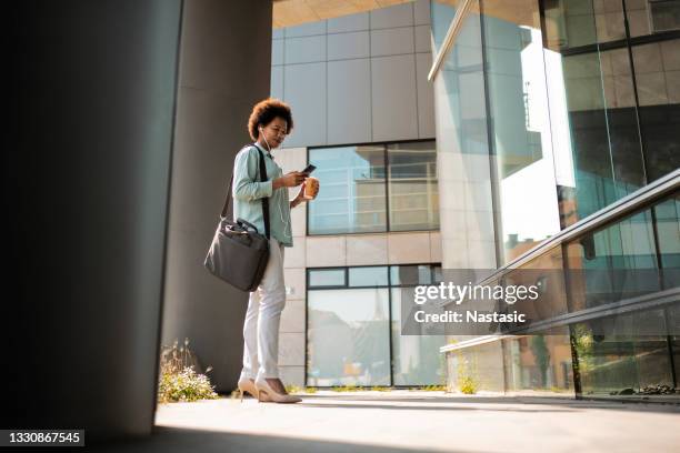 joven afroamericana en una pausa para el café mirando el teléfono inteligente con auriculares - maletín para portátil fotografías e imágenes de stock