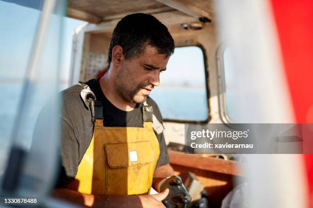 pêcheur debout dans pilothouse enlever les gants de travail - pêcheur photos et images de collection
