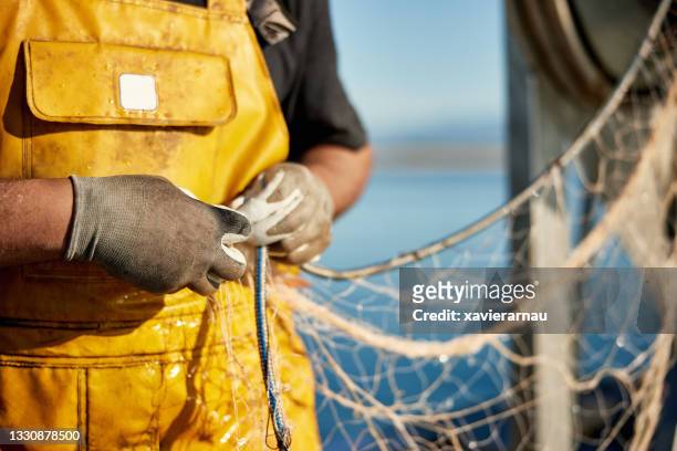fisherman in protective workwear managing trawl net - kommersiellt fisknät bildbanksfoton och bilder