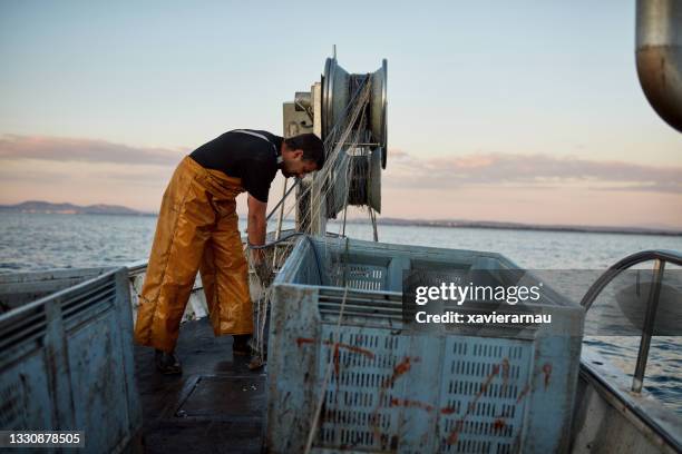 pescador caucásico que trabaja con red de arrastre en la madrugada - fishing boat fotografías e imágenes de stock