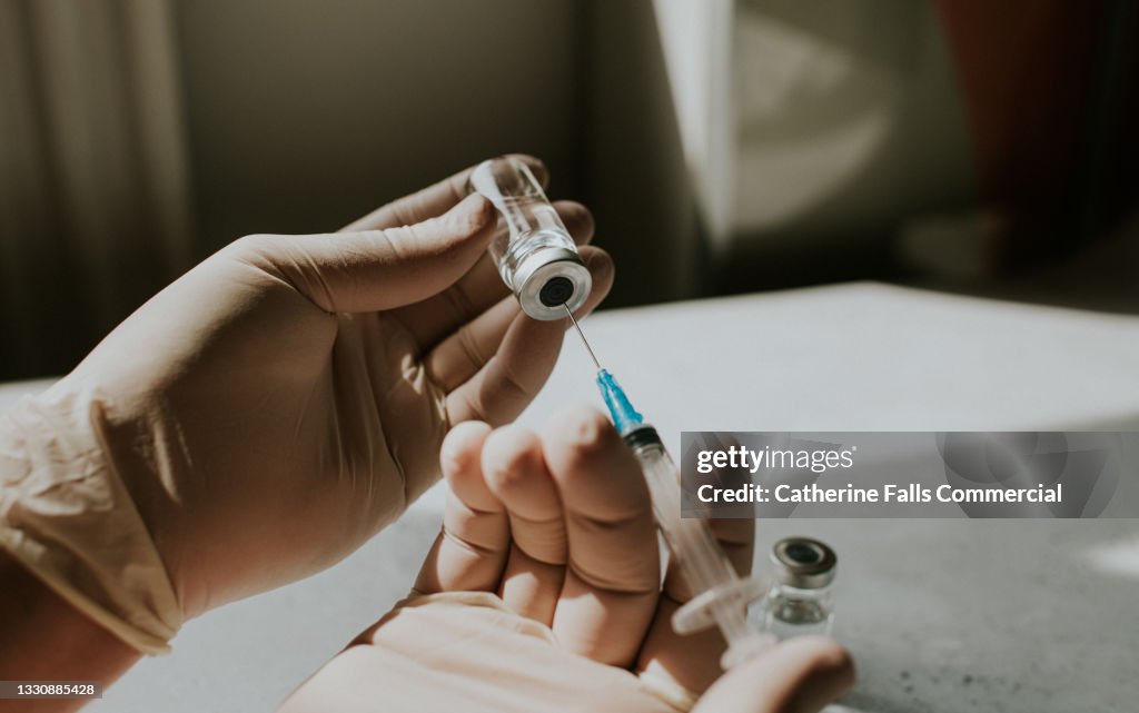 Gloved hand holds a syringe and a phial - Conceptual medical image with space for copy.