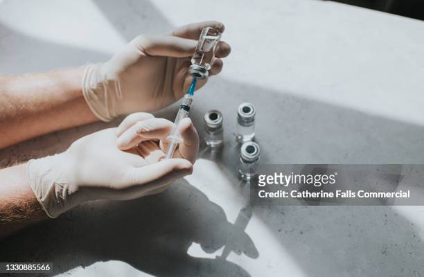 gloved hand holds a syringe and a phial - conceptual medical image with space for copy. - pharmaceutical stockfoto's en -beelden