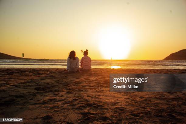 two young woman looking at the ocean in the late afternoon - friends sunset stockfoto's en -beelden