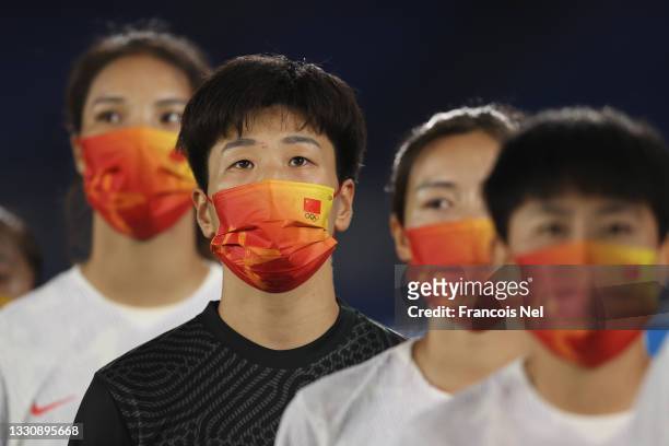 Shimeng Peng of Team China wears a face mask with teammates as they stand for the national anthem prior to the Women's Group F match between...