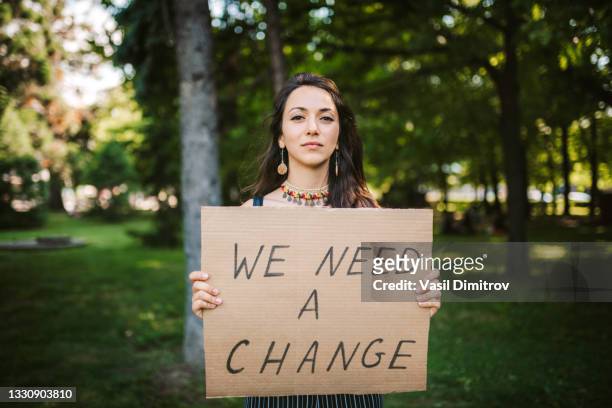 junge aktivistin / demonstrantin mit einem "we need change"-plakat - protest stock-fotos und bilder