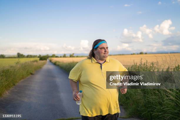 overweight man jogging while listening to music - fat guy stock pictures, royalty-free photos & images