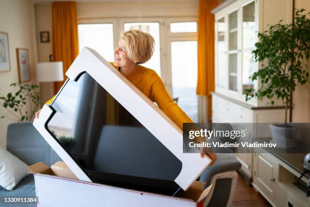 a happy woman receives and opens her online purchase of electrical equipment - new television stock pictures, royalty-free photos & images
