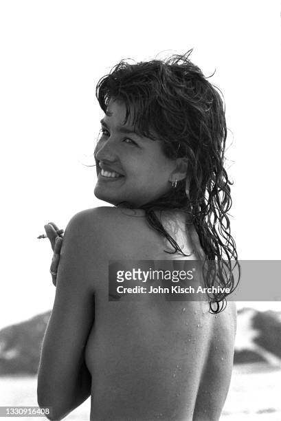 Portrait of American model and actress Janice Dickinson, topless and with a cigarette in one hand, as she looks over her shoulder, Southampton, New...