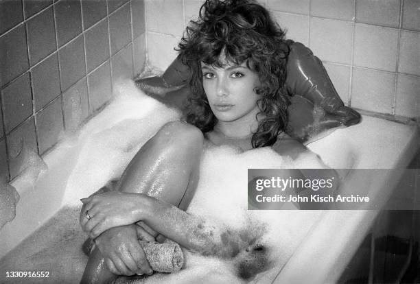 Portrait of American-British actress and model Kelly LeBrock, partially covered with soap bubbles, as she poses in a bathtub, New York, 1982.