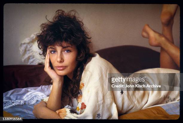 Portrait of American-British actress and model Kelly LeBrock, dressed in a robe, as she lays on a bed, her chin in her palm, New York, 1981.