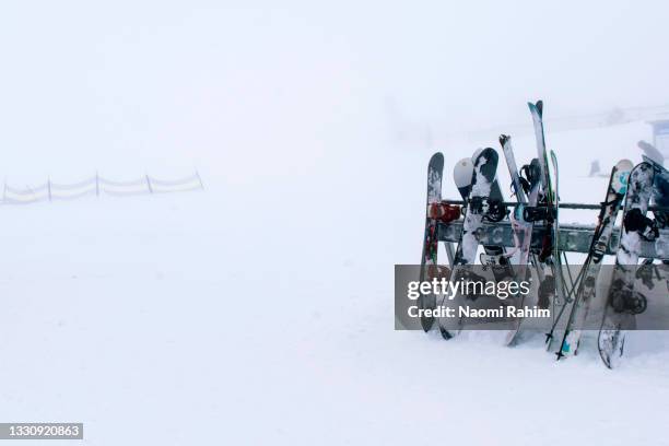 snowboards, skis and poles leaning against ski rack on snow field - winter skiing australia stock-fotos und bilder