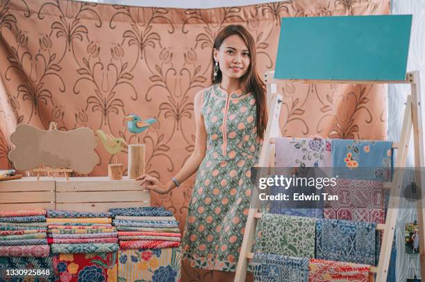 malaysian chinese beautiful woman portrait in front of her batik fabric textile collection  retail store looking at camera smiling - batik design stock pictures, royalty-free photos & images