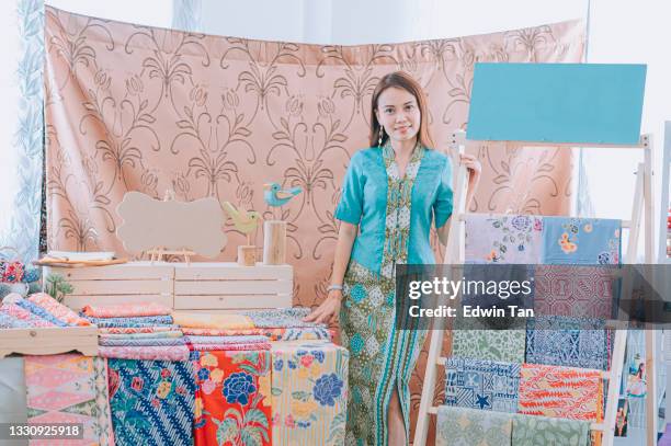 malaysische chinesische schöne frau porträt vor ihrem batik stoff textil kollektion einzelhandelsgeschäft mit blick auf die kamera lächelnd - traditioneller batikstil stock-fotos und bilder