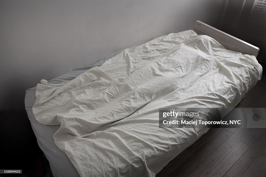 Woman's body covered with white sheet on bed.