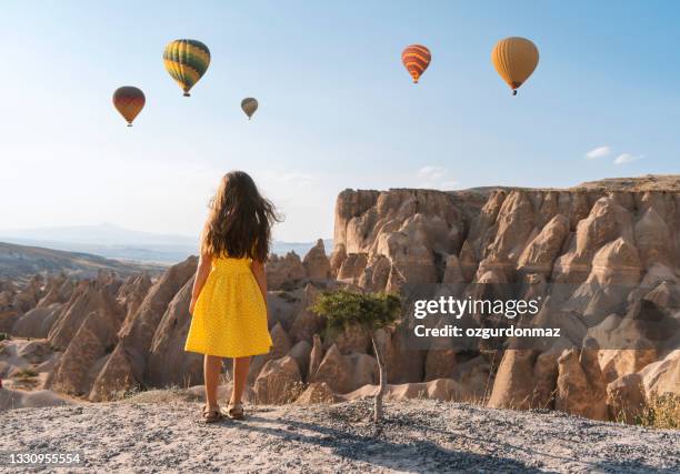 cute little girl in a yellow dress watching hot air balloons in cappadocia, turkey - capadócia imagens e fotografias de stock