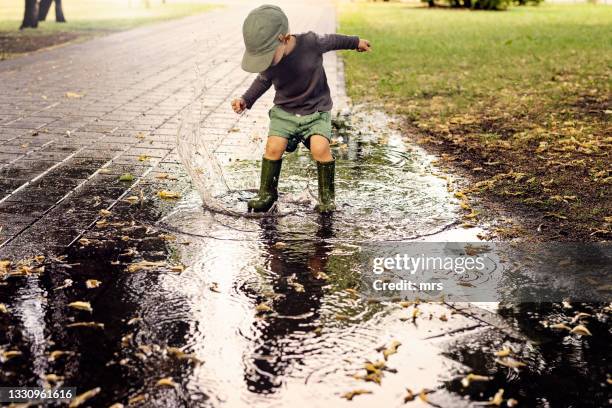 little boy splashing water in puddle - standing water fotografías e imágenes de stock