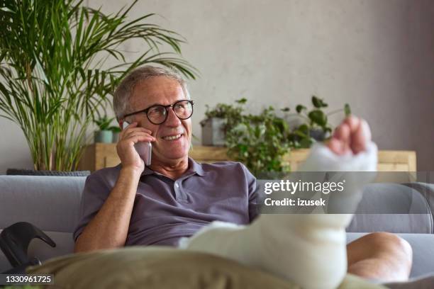 senior man with broken leg at home - bandage stockfoto's en -beelden