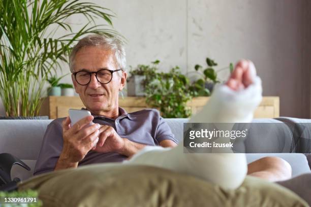 älterer mann mit gebrochenem bein zu hause - gipsverband stock-fotos und bilder