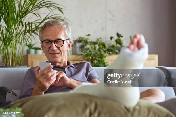 uomo anziano con gamba rotta in casa - injured foto e immagini stock