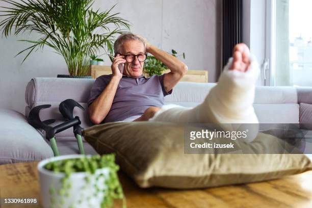 älterer mann mit gebrochenem bein zu hause - gipsbein stock-fotos und bilder