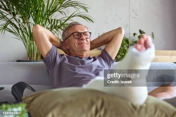 senior man with broken leg at home - raised hand to foot pose stock pictures, royalty-free photos & images
