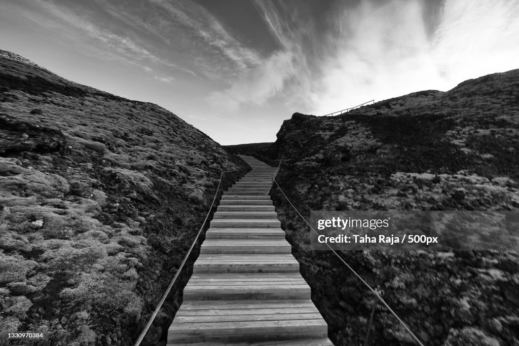 Empty footpath leading towards mountains against sky